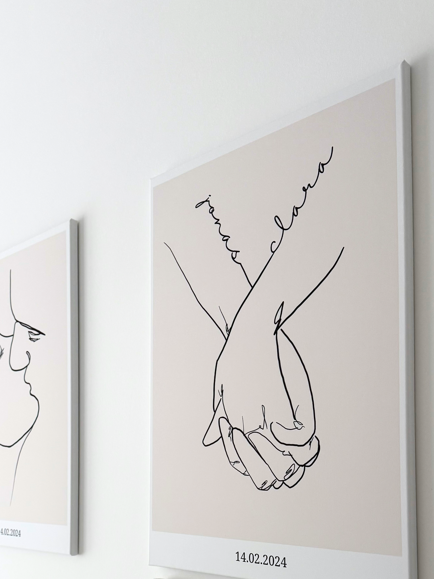 Zwei personalisierte Leinwandbilder von Sels Studio: links eine minimalistische Line Art Zeichnung eines küssenden Paares, rechts ein Hand-in-Hand-Motiv mit Namen und dem Datum , beide auf beiger Leinwand an einer weißen Wand.