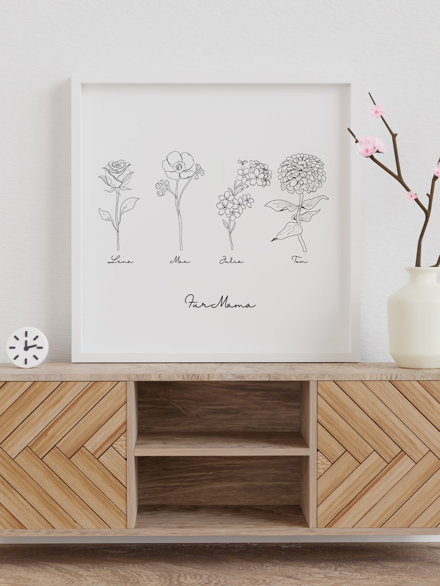Ein quadratisches, gerahmtes Poster von Sels Studio im minimalistischen line art-Stil steht auf einem Holzsideboard mit Fischgrätmuster. Die schwarz-weiße Illustration zeigt vier fein gezeichnete Blumen mit je einem Vornamen darunter („Lena“, „Max“, „Julia“, „Tom“), ergänzt durch die Widmung „Für Mama“ in eleganter Handschrift. Das reduzierte Design hebt die florale Symbolik hervor und eignet sich ideal als personalisiertes Geschenk zum Muttertag. 